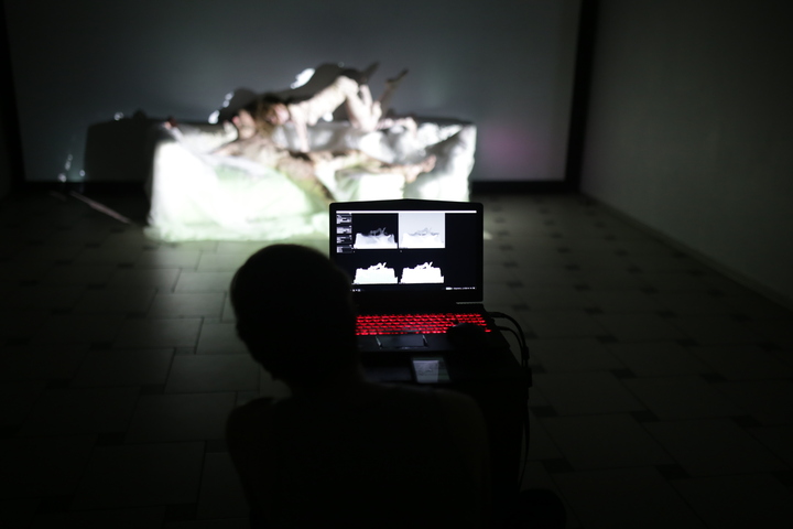 A silhouetted visitor views a laptop showing depth-camera silhouette feeds, facing a lit sculptural installation.