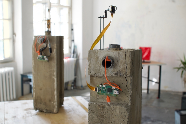 Close-up of a concrete pillar embedded with a Raspberry Pi Zero, orange cables and a camera on a mounting arm.